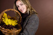 A woman holding a basket of conkers, acorns and autumn leaves