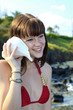 girl in a bikini listening to a sea shell at a hawaii beach