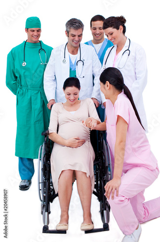 Photo: Brunette pregnant woman sitting on wheelchair and a medical team Brunette pregnant woman sitting on wheelchair and a medical team