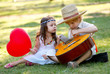 Young couple with guitar on grass in park
