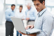 Young executive using a laptop with coworker at the back