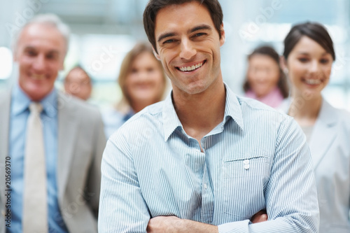 Foto: Confident smiling business man with his team at the back Confident smiling business man with his team at the back