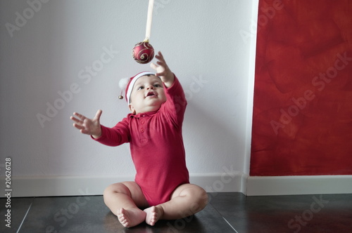 Photo: Baby boy sitting on floor reaching for Christmas ball Baby boy sitting on floor reaching for Christmas ball