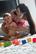 Young woman and baby boy sitting on rug playing with toys