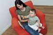 Young woman and baby boy sitting on arm chair with a book