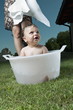 Baby boy taking bath in tub in garden and young woman waist down with towel
