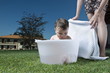 Baby boy taking bath in tub in garden and young woman waist down with towel