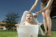 Baby boy taking bath in tub in garden and young woman waist down with towel