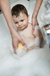 Baby boy taking bath in tub, young woman's hands washing him with sponge
