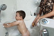 Baby boy taking bath in tub, partial view of young woman washing him with sponge