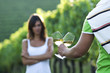 Young woman in vineyard, man bringing glasses of white wine