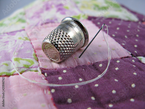 Photo: Silver colored thimble on an old antique patchwork quilt Silver colored thimble on an old antique patchwork quilt