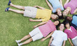 Teenagers lying on grass with their heads together in circle