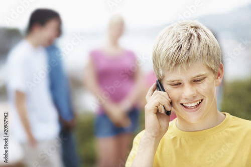 Foto: Closeup of boy talking on cellphone with friends in background Closeup of boy talking on cellphone with friends in background