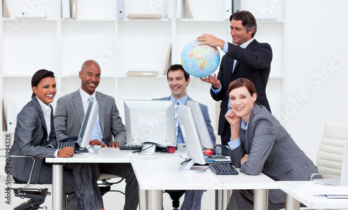 Photo: Smiling manager holding a globe with his team working at compute Smiling manager holding a globe with his team working at compute