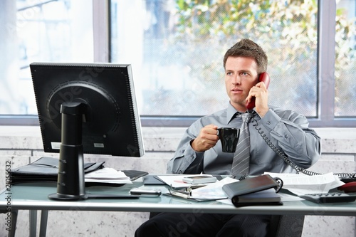 Photo: Businessman calling at office with mug Businessman calling at office with mug