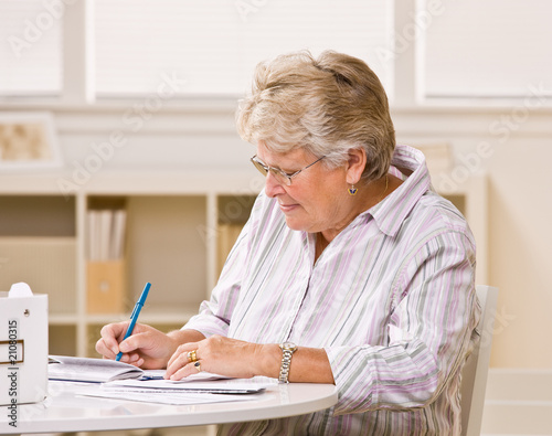 Photo: Senior woman writing checks Senior woman writing checks
