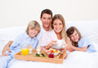 Foto: Smiling family having breakfast sitting on bed Smiling family having breakfast sitting on bed