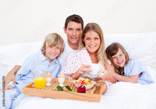 Foto: Smiling family having breakfast sitting on bed Smiling family having breakfast sitting on bed
