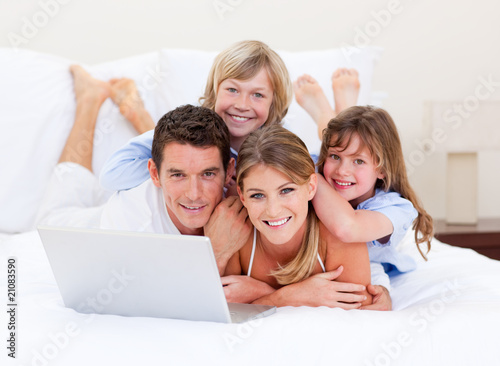 Photo: Smiling family looking at a laptop lying down on bed Smiling family looking at a laptop lying down on bed
