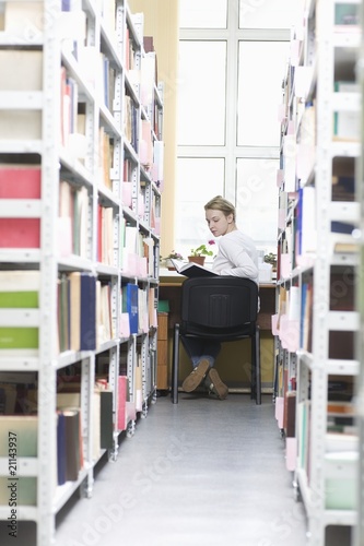 Foto: Young woman sits at desk in library Young woman sits at desk in library
