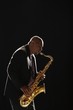 Man stands playing saxophone against black background