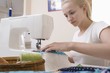 Young woman sits making patchwork at sewing machine