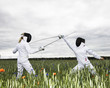 Two girls fencing in a field.