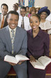 young couple with bibles sitting on church pews portrait