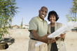middle-aged couple holding blueprints in vacant lot portrait