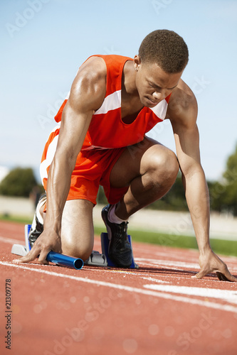Photo: runner waiting in starting block holding baton runner waiting in starting block holding baton