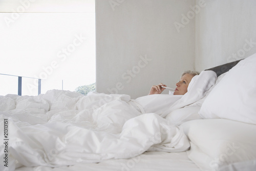Photo: mature woman lying in bed with thermometer in mouth side view mature woman lying in bed with thermometer in mouth side view