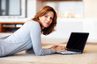 Pretty young woman using laptop while lying on floor