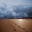 Dark storm shown behind prints on a beach