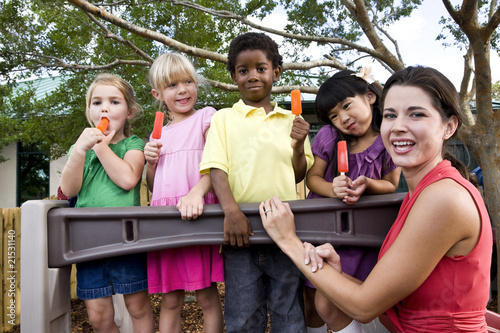 Photo: Preschool children playing on playground with teacher Preschool children playing on playground with teacher