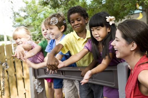 Photo: Preschool children playing on playground with teacher Preschool children playing on playground with teacher