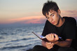 teenager boy reads book sitting on beach in evening