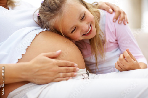 Foto: Excited young girl listening to her pregnant mother belly Excited young girl listening to her pregnant mother belly