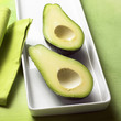 Two avocado halves on white platter; green background