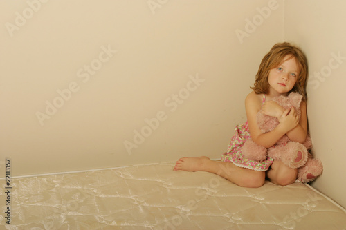 Photo: Sad girl sitting on an old mattress holding bear Sad girl sitting on an old mattress holding bear