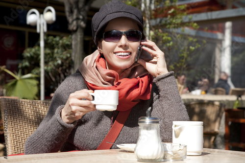 Photo: Young woman sits in the summer cafe and speaks by phone Young woman sits in the summer cafe and speaks by phone