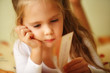 closeup of a little girl reading a book on her bed