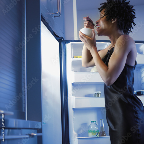 Photo: African woman eating next to open refrigerator African woman eating next to open refrigerator