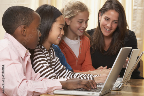 Photo: Multi-ethnic children and teacher typing looking at laptops Multi-ethnic children and teacher typing looking at laptops