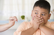 Hispanic boy covering mouth next to broccoli