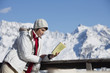 Young woman reading a book, enjoying winter sun, mountains in background