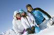 Couple and daughter sitting in snow, smiling at camera