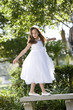 Photo: Beautiful child wearing white dress playing on park bench Beautiful child wearing white dress playing on park bench