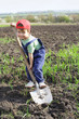 Little boy on field with big shovel, looking to camera