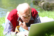 Alter Mann arbeitet mit dem Laptop im Grünen am Wasser